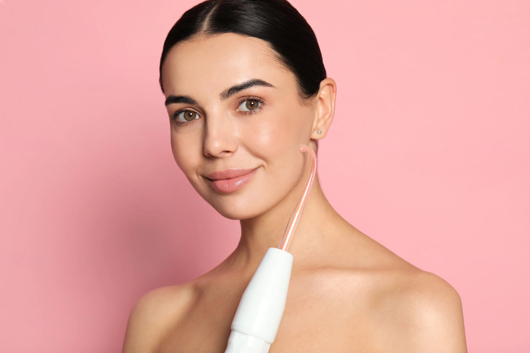 pink background woman using high frequency wand on cheeck